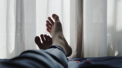 Man laying on the bed relaxing and chilling by moving his feet into the rhythm of music.