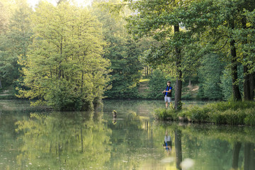 Fototapeta na wymiar Man fishing in the green wilderness with lush forest on a sunny summer day at sunset.