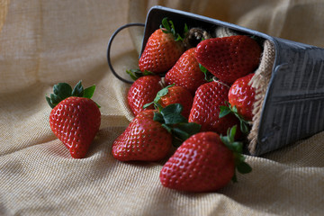Strawberries in an antique metal container on a rustic cloth.
