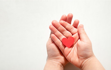 Red heart is cut out of paper in the hands of a child on a white background
