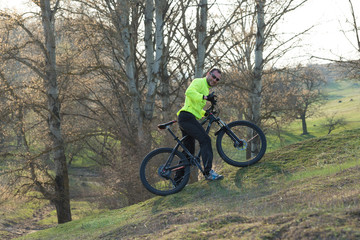 Cyclist in pants and green jacket on a modern carbon hardtail bike with an air suspension fork. The guy on the top of the hill rides a bike.