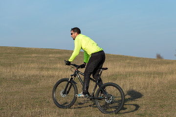 Obraz premium Cyclist in pants and green jacket on a modern carbon hardtail bike with an air suspension fork. The guy on the top of the hill rides a bike.