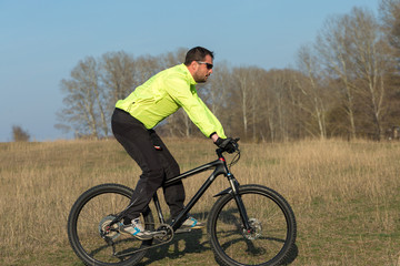 Cyclist in pants and green jacket on a modern carbon hardtail bike with an air suspension fork. The guy on the top of the hill rides a bike.