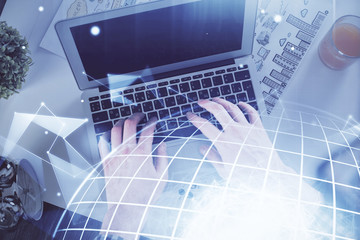 Multi exposure of man's hands typing over computer keyboard and world map hologram drawing. Top view. Technology concept.