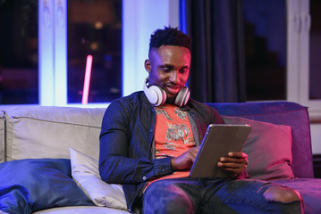 Handsome joyful stylish african american with headphones on his neck relaxing on the soft sofa at...