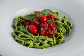Spaghetti pasta with homemade spinach sauce, green spaghetti, fried tomatoes and fresh basil leaves, vegetarian foodclose-up