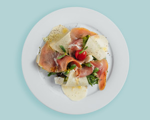 salad with prosciutto pear slices, tomatoes and herbs on a white plate, top view, top