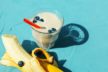 Glass of banana milkshake or smoothie on blue background