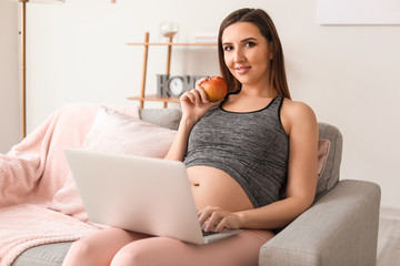 Beautiful pregnant woman with laptop and apple at home