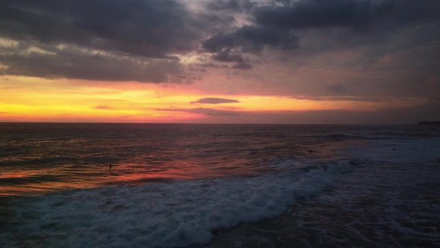 a tropical sunset filmed from above with the drone. An orange sky full of clouds. The rays of the sunset are reflected in the water and the waves of the ocean.