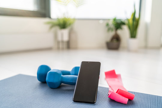Fitness at home workout exercises online on smartphone app for training indoors at apartment with dumbbells weight and resistance bands in living room.