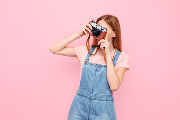 stylish young girl takes photos with a retro camera isolated on a pink background