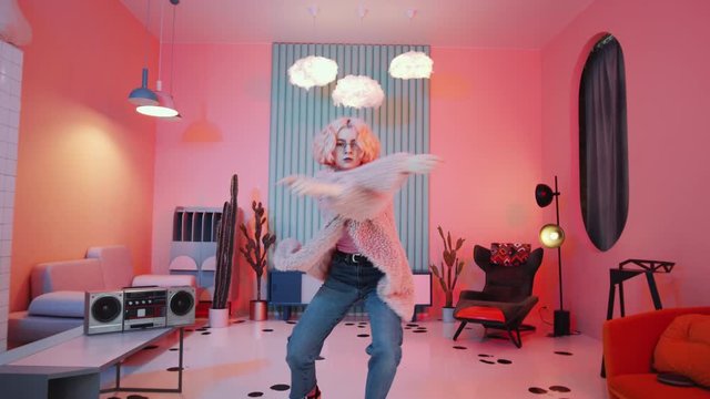 Young blonde female dancer in glamorous outfit dancing vogue for camera in trendy studio with vintage interior and pink neon light