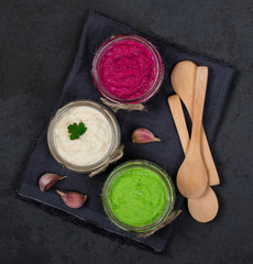 Obraz na płótnie Canvas Russian appetizer horseradish with beetroot, green horseradish wasabi, white horseradish with lemon in jars on a linen napkin on a dark background top view