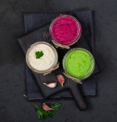 Russian appetizer horseradish with beetroot, green horseradish wasabi, white horseradish with lemon in jars on a wooden Board on a dark background top view