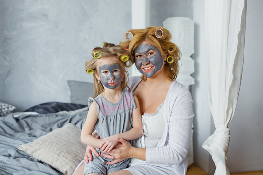 Happy Mother And Daughter With Black Face Masks In The Bedroom On The Bed. The Concept Of Home Entertainment.