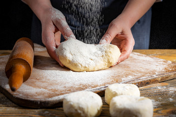 Female hands knead the dough on a wooden antique table on a dark background, close-up, shallow depth of field, beautiful directional lighting. Concept of home baking and comfort.