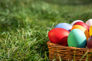 Multi-colored Easter eggs in a basket on the grass, the background is blurred, shallow depth of field, selective focus. Easter holiday concept