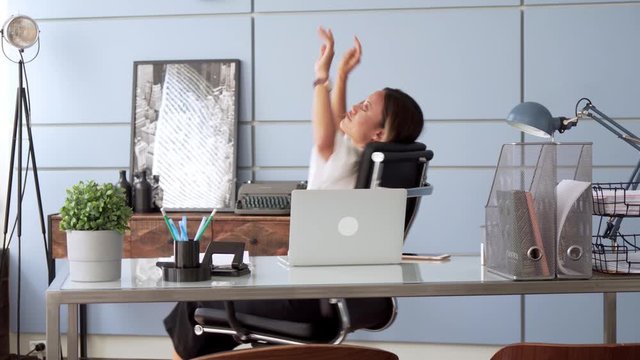 young elegant woman sits at table with laptop, smiling. looks independent, focused and confident. business woman working in modern office, spins around on chair