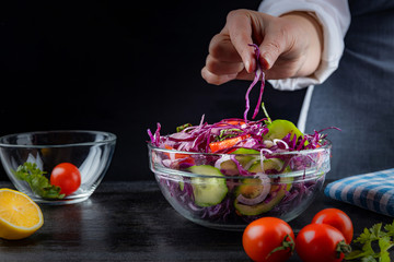 Making a salad, female hands mix vegetable salad, close-up on a dark background, shallow depth of field. Healthy food concept.