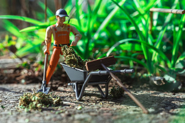 Worker is cleaning weed with wheelbarrow, shovel and broom.