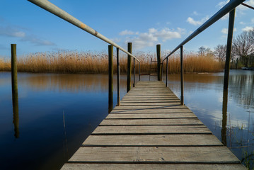 boardwalk on a landing bridge at the canal Hartwarder Außentief (municipality Stadland-Rodenkirchen, district Wesermarsch, Germany) over tranquil blue water against vivid blue sky