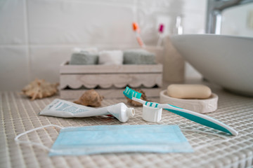 Fototapeta na wymiar Open toothpaste, a toothbrush, and a medical mask that has been removed from your face are lying on the table in front of the washbasin