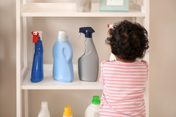 Little African-American baby playing with washing liquids at home. Child in danger