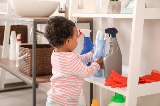 Little African-American baby playing with washing liquids at home. Child in danger