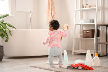 Little African-American baby playing with washing liquids at home. Child in danger