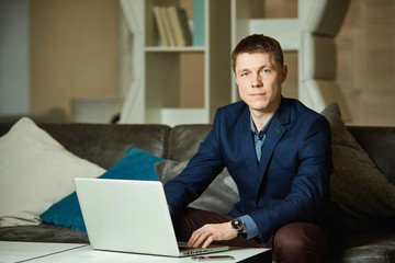 Portrait of a young businessman sitting at a table and typing on a laptop, looking at camera.