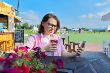 Fototapeta premium Summer portrait of mature woman with drink and smartphone