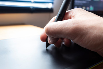 Close up to a male hand holding up a black digital pencil over a black and green drawing tablet in desk and home office background. Ideal for graphic design, web and every relationated with technology