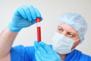 a test tube with a blood sample in the hands of a doctor in blue rubber gloves and a mask on a light background. Concept of coronavirus, covid-19