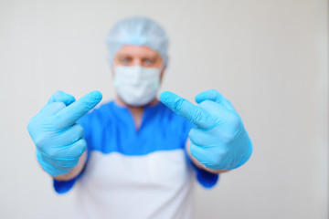 a young male doctor shows his middle finger in rubber gloves against a light background. Stopping the disease, coronavirus, covid-19