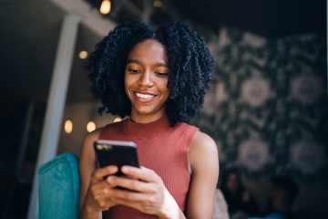 Black happy carefree lady chatting with friend on phone in cafeteria