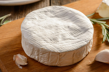 Closeup on a Brie cheese wheel, garlic and rosemary