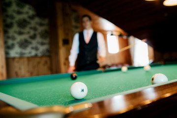 elegant young man in a dark suit plays billiards