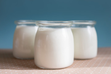 Obraz na płótnie Canvas three glass jars of milk product on a cute polka dot tablecloth, blue background