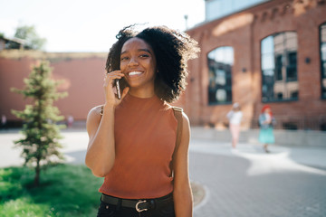 Young pleased African American woman talking on smartphone at college