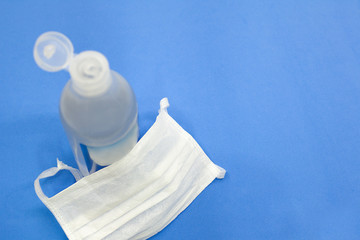 Máscara protetora e álcool em gel para proteção contra o coronavírus 
 em fundo azul.