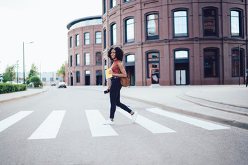 Cheerful young female student crossing zebra in city