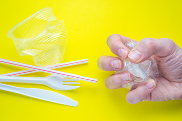 Hand holding plastic waste on a yellow background representing the concept of recycling and environmental sustainability.