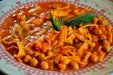 Italian pasta with chickpeas in tomato sauce, seasoned with olive oil and decorated with sage and rosemary.