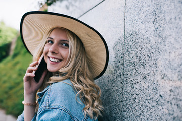 Cheerful woman speaking on smartphone near wall