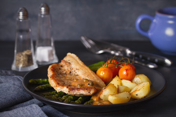 Roast pork chop with vegetables on black plate. horizontal image