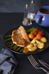 Roast pork chop with vegetables on black plate. vertical image