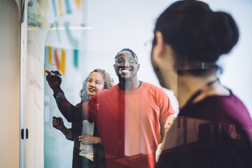 Satisfied colleagues using sticky notes on glass at office