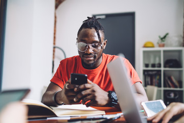 Young casual man sitting at table and using smartphone