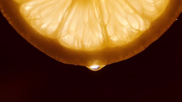 Water pouring on half slice cut of fresh lemon against black background